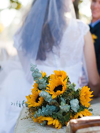 Bride and groom in the background, bouquet of sun flowers in the foreground