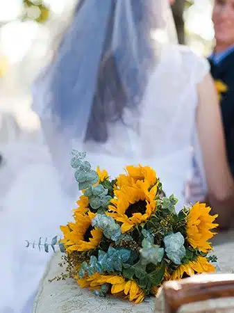 Bride and groom in the background, bouquet of sun flowers in the foreground