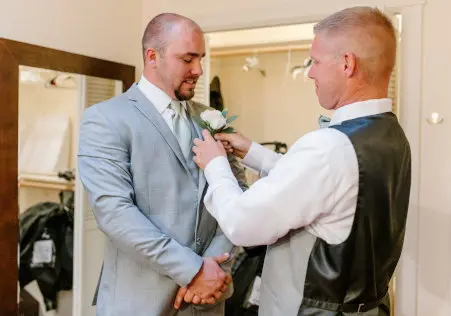 The best man fulfills one of his bridal party roles by helping his friend affix his boutonniere. Photo by Katelyn Bradley Photography