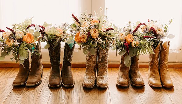 Photo of the bride and bridesmaid's cowboy boots with autumn floral arrangements by Lela Spiva Photography