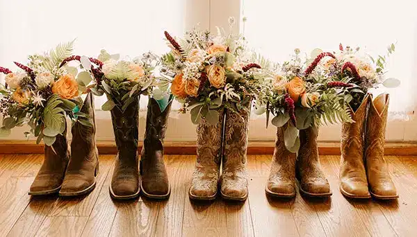 Photo of the bride and bridesmaid's cowboy boots with autumn floral arrangements by Lela Spiva Photography