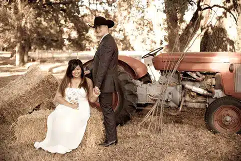 A bride and groom pose by an old tractor to bring their rustic theme together
