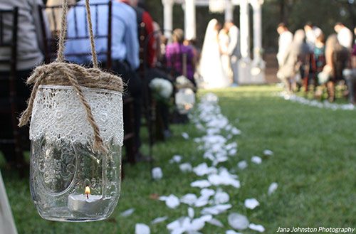 Candles inside mason jars line the aisle during a wedding ceremony. Photo by Jana Johnston Photography