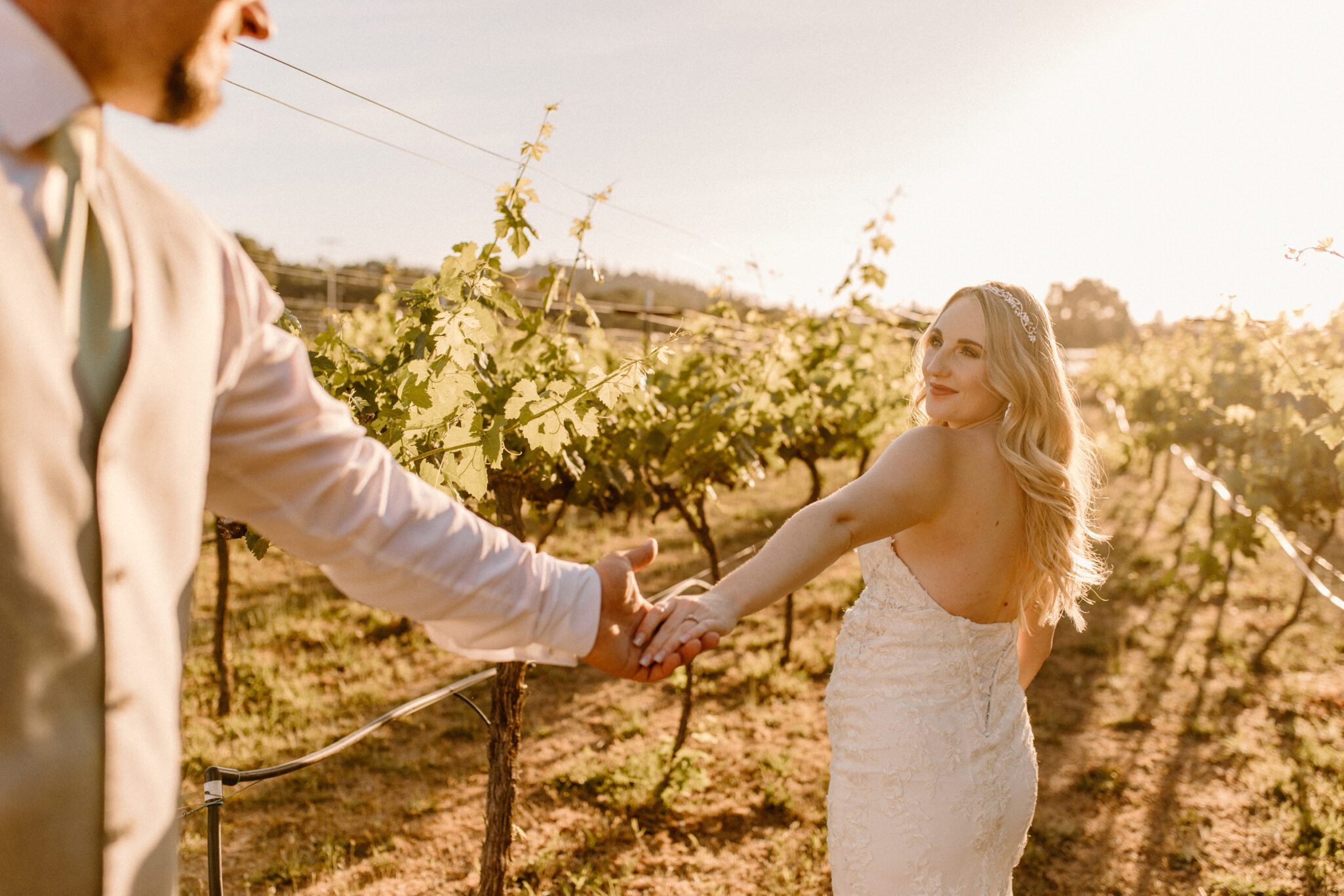 close up of bride smiling looking back at groom in vineyard at sunset 