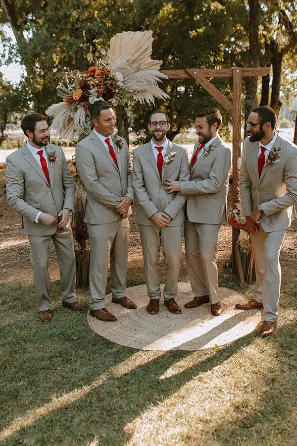 the groomsmen smiling at the groom under the flowered wedding arch