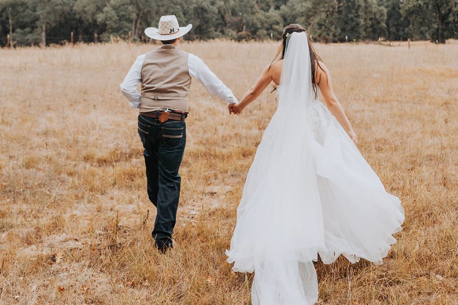 bride and groom walking away into a field