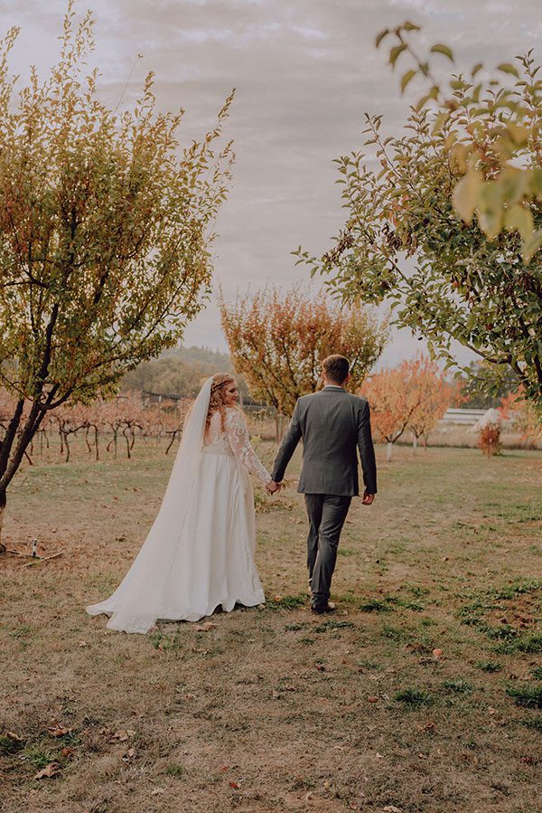 Bride and groom wander through field holding hands