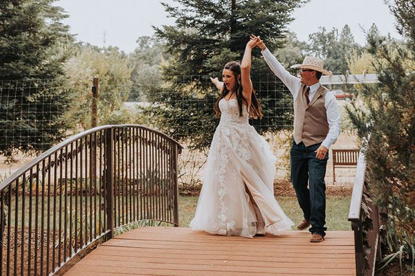 Groom in a cowboy hat twirls his bride on the footbridge. Photo by Taylor Jean Photography