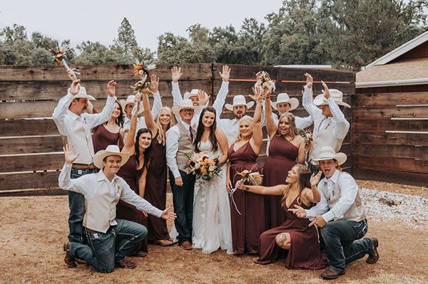 Wedding party strike funny poses by a wooden fence. Photo by Taylor Jean Photography