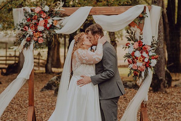 Bride and groom kiss under the oaks by their wedding arch.  Photo by Dream Capture Studios