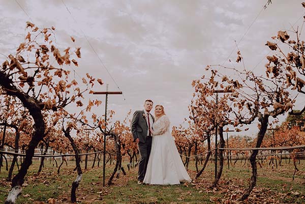 Groom and bride pose in vineyards on a cloudy day. Photo by Dream Capture Studios