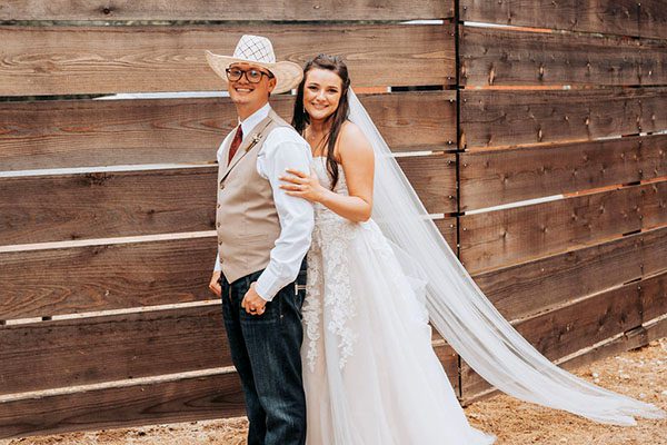Groom and bride in country-themed wedding pose by a wooden fence. Photo by Taylor Jean Photography