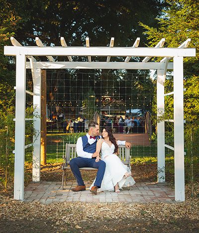 Happy couple seated under a white pergola in the garden. Photo by Camden Ashley Photography 