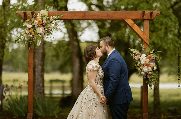 Newly married couple kiss by a wedding arch. Photo by Heidi Peinthor Photography