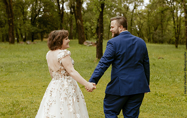 A happy bride and groom holding hands as they walk away from the camera. Photo by Heidi Peinthor Photography