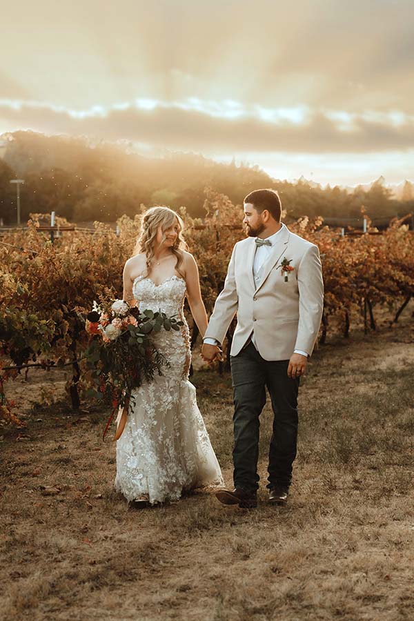 Maddy and Kasey hold hands while walking through the vineyard. Photo by Dream Capture Studios