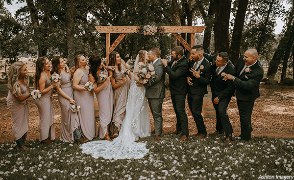 Bridesmaids and groomsmen watching the happy couple kiss. Photo by Ashton Imagery