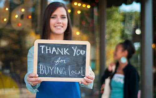 Young woman holding a sign that reads, 'Thank you for buying local'