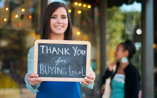 Young woman holding a sign that reads, 'Thank you for buying local'