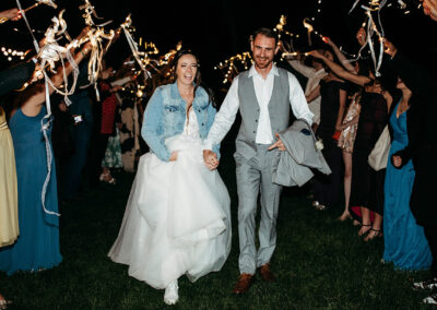 Bride and groom happily walking through lights and wands from guests. Photo by Eden Oaks Photography