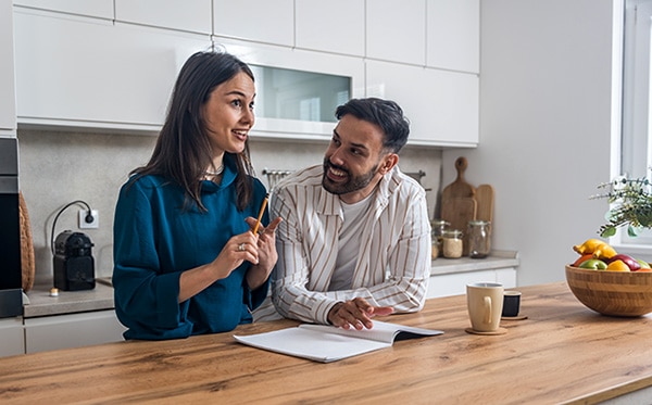 Young engaged couple standing together in their kitchen, figuring out how to plan a wedding on a budget while smiling and preparing for their upcoming celebration