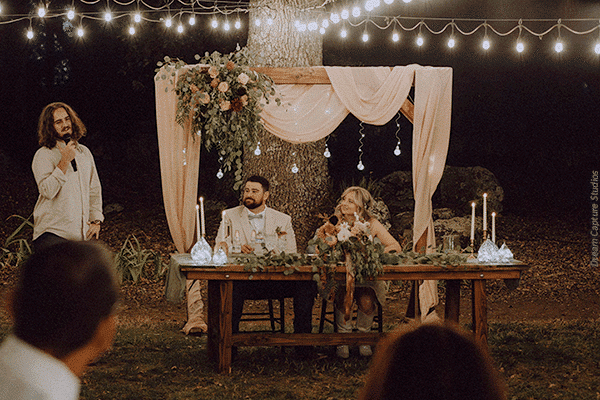 A couple listening to a groomsman give a speech at their wedding. Photo by Dream Capture Studios